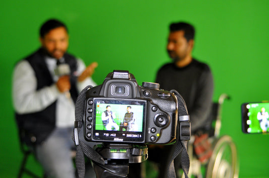 two men talking to camera in front of a green screen